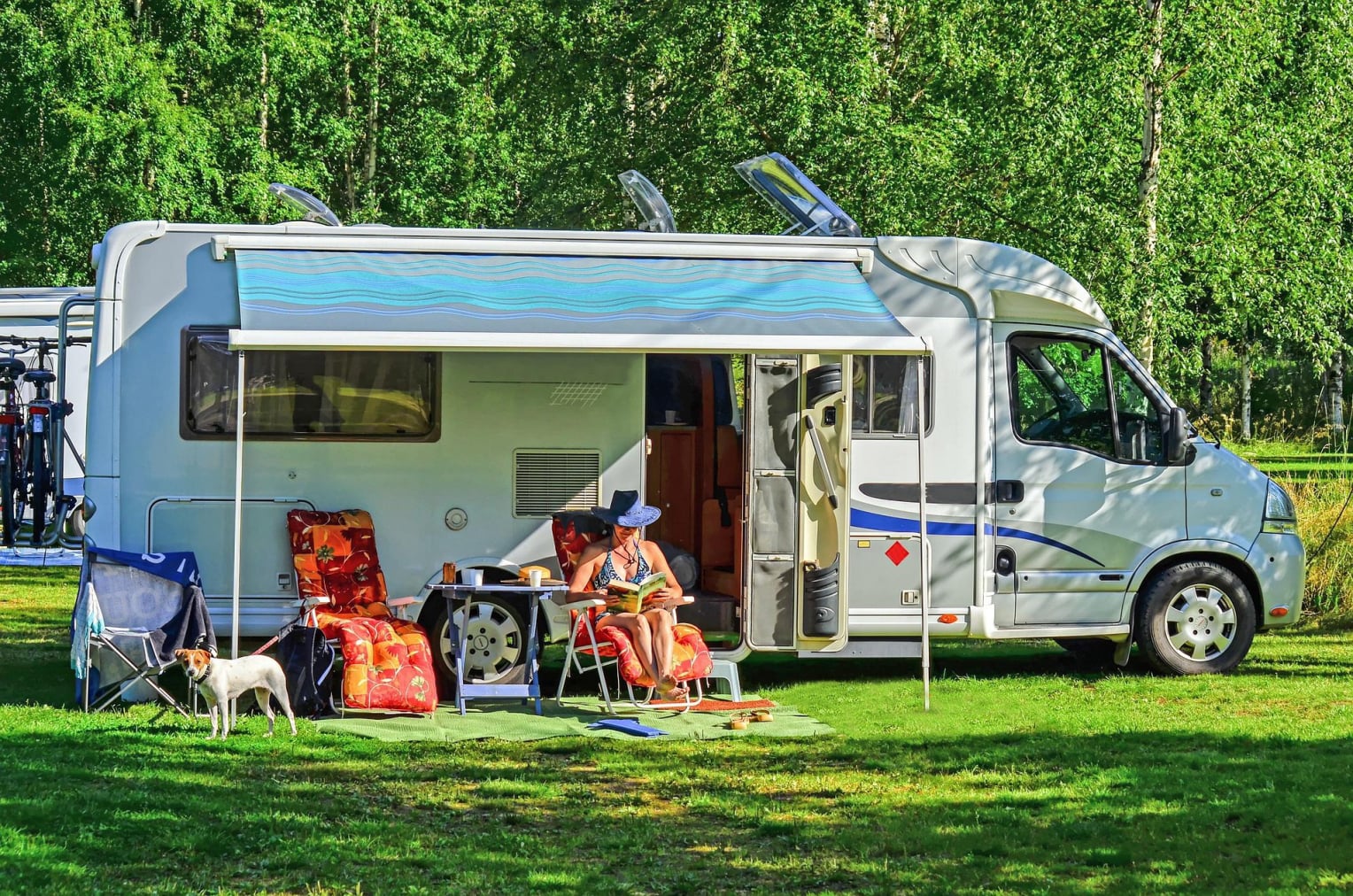 RV camper set up in a camp site with and woman sitting in a chair, and a dog on a leash